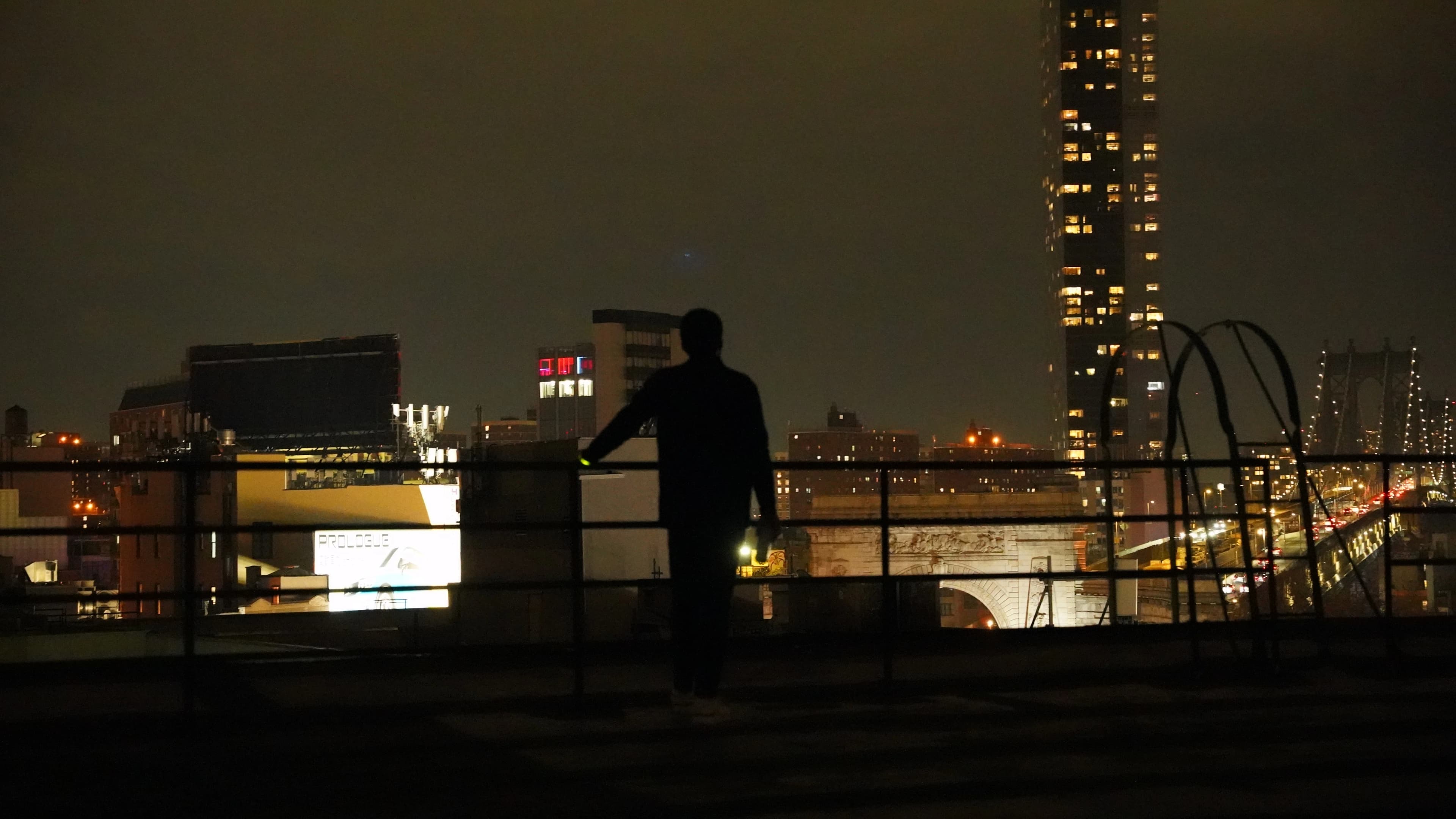 A figure looks out over a city skyline at night before a Love Science evening